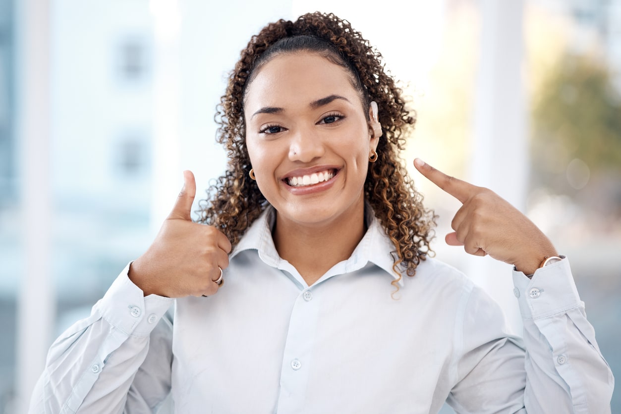 Smiling woman pointing to her new hearing aid.