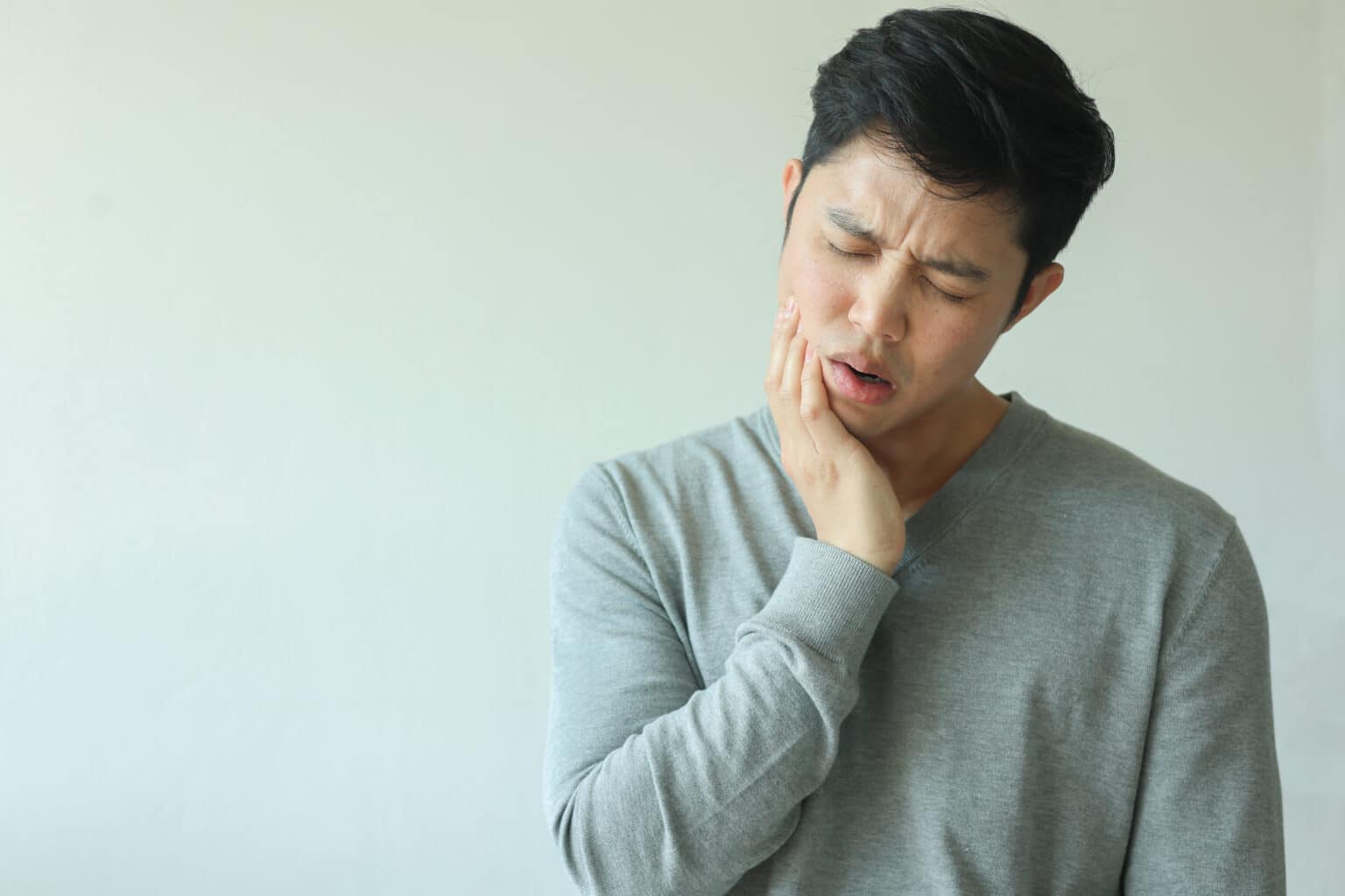 A man looks uncomfortable and holds his jaw due to TMJ pain.
