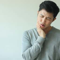 A man looks uncomfortable and holds his jaw due to TMJ pain.