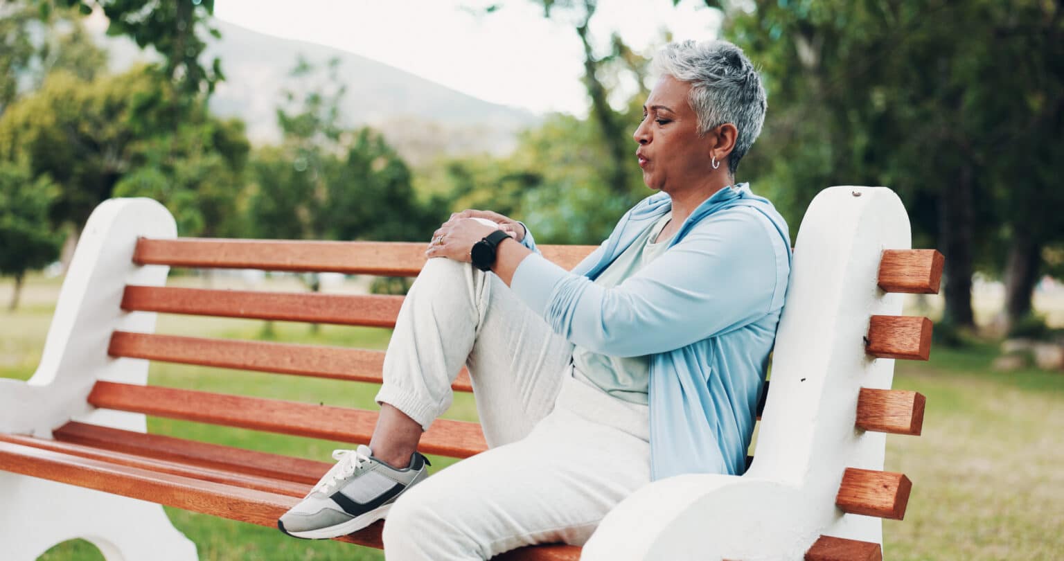 Arthritic woman massages her knee on a park bench