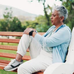 Arthritic woman massages her knee on a park bench