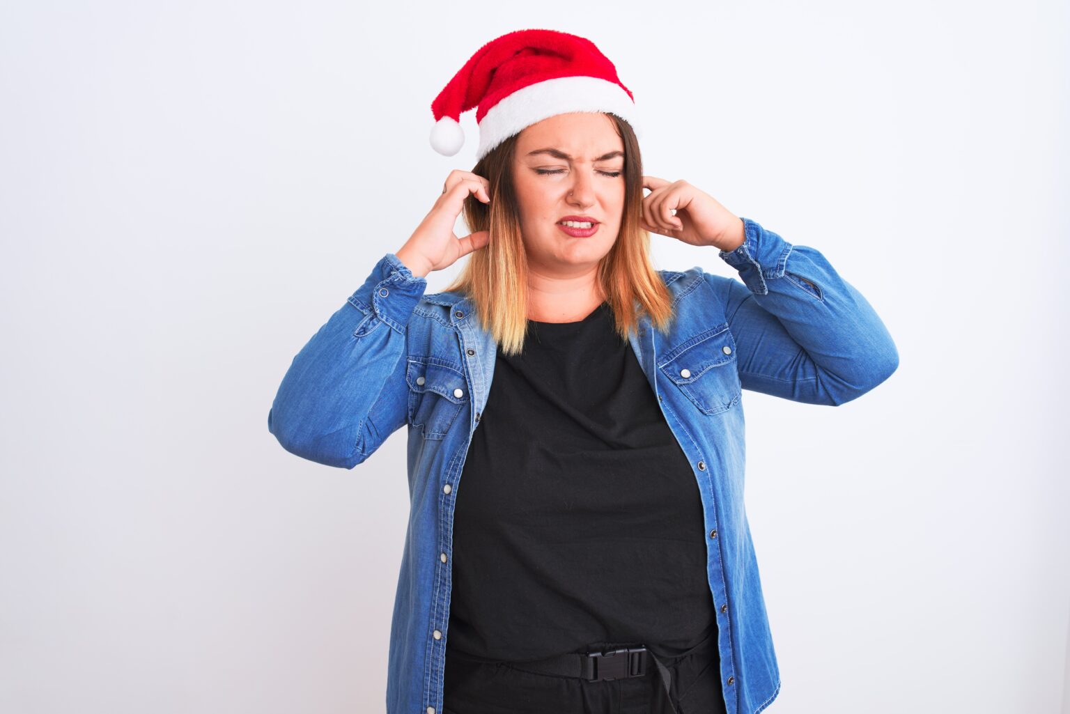 Person wearing a Santa hat is suffering from tinnitus and holding their ears