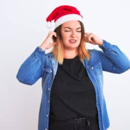 Person wearing a Santa hat is suffering from tinnitus and holding their ears