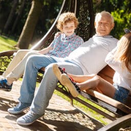 Grandfather with his two grandkids sitting on a bench in a park on a beautiful day.