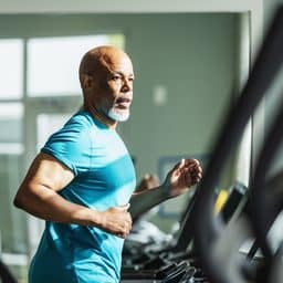 A senior man working out at the gym, running on a treadmill.