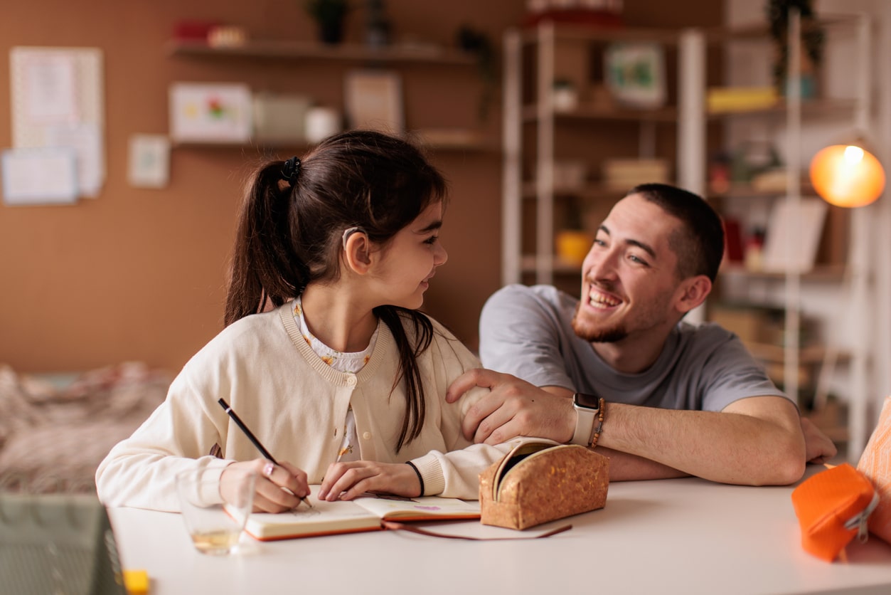 Child with hearing aid working on homework with her parent.